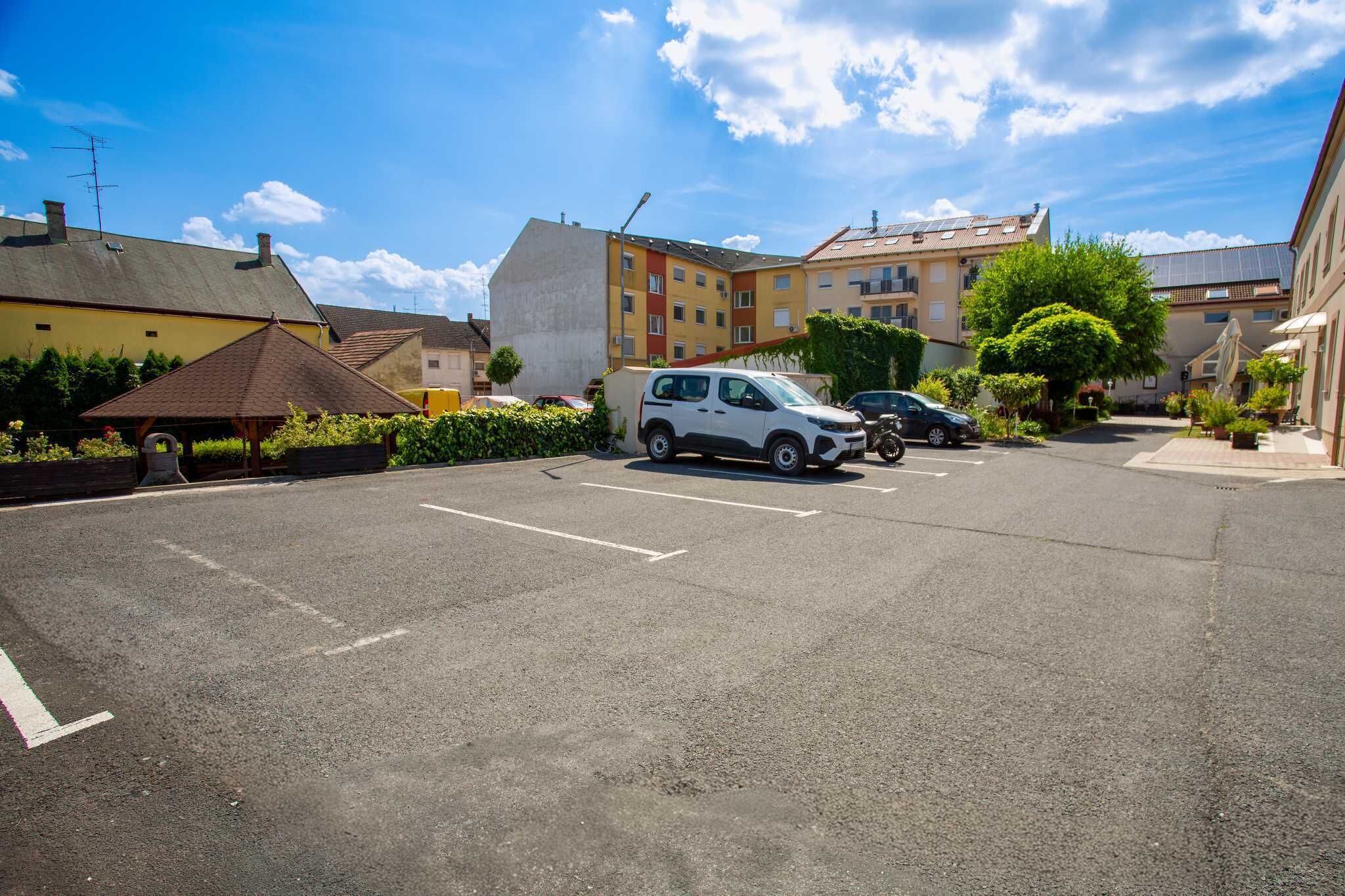 A parking lot with multiple cars, a building with a sloped roof, and a clear sky.