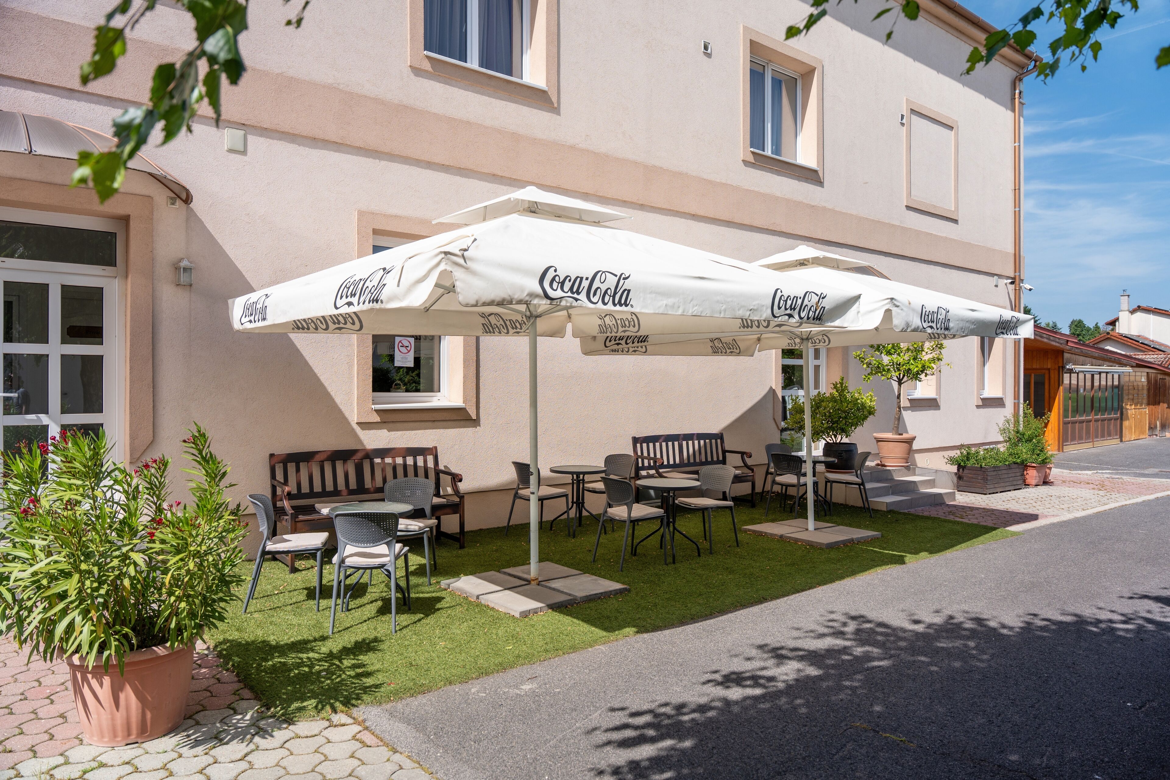An outdoor seating area with Coca-Cola branded umbrellas, a patio with chairs and tables, and a building with a beige facade.
