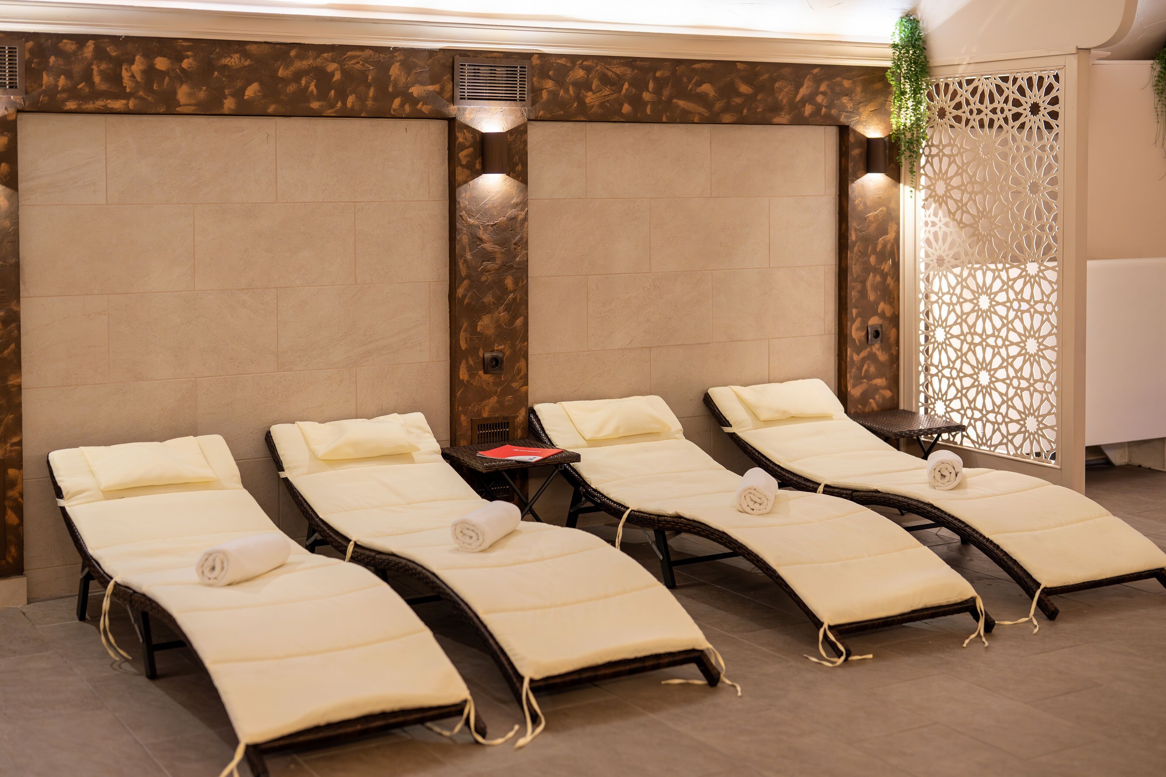 A spa room with four sun loungers, a small table with a red book, and a decorative wall panel.