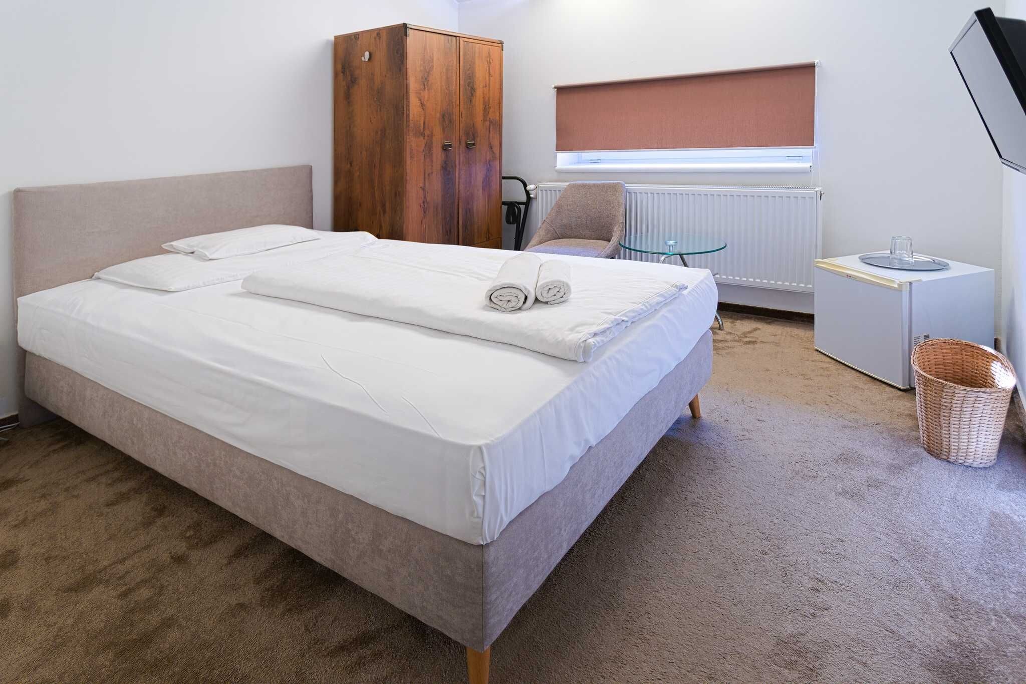 Un dormitorio con cama, armario de madera, escritorio, silla, radiador y ventana con persianas.