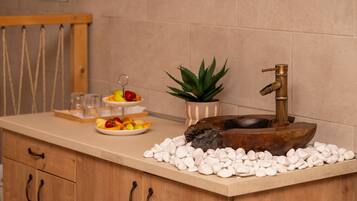 A kitchen counter with a wooden sink, white pebbles, a fruit platter, a potted plant, and a hanging rack.