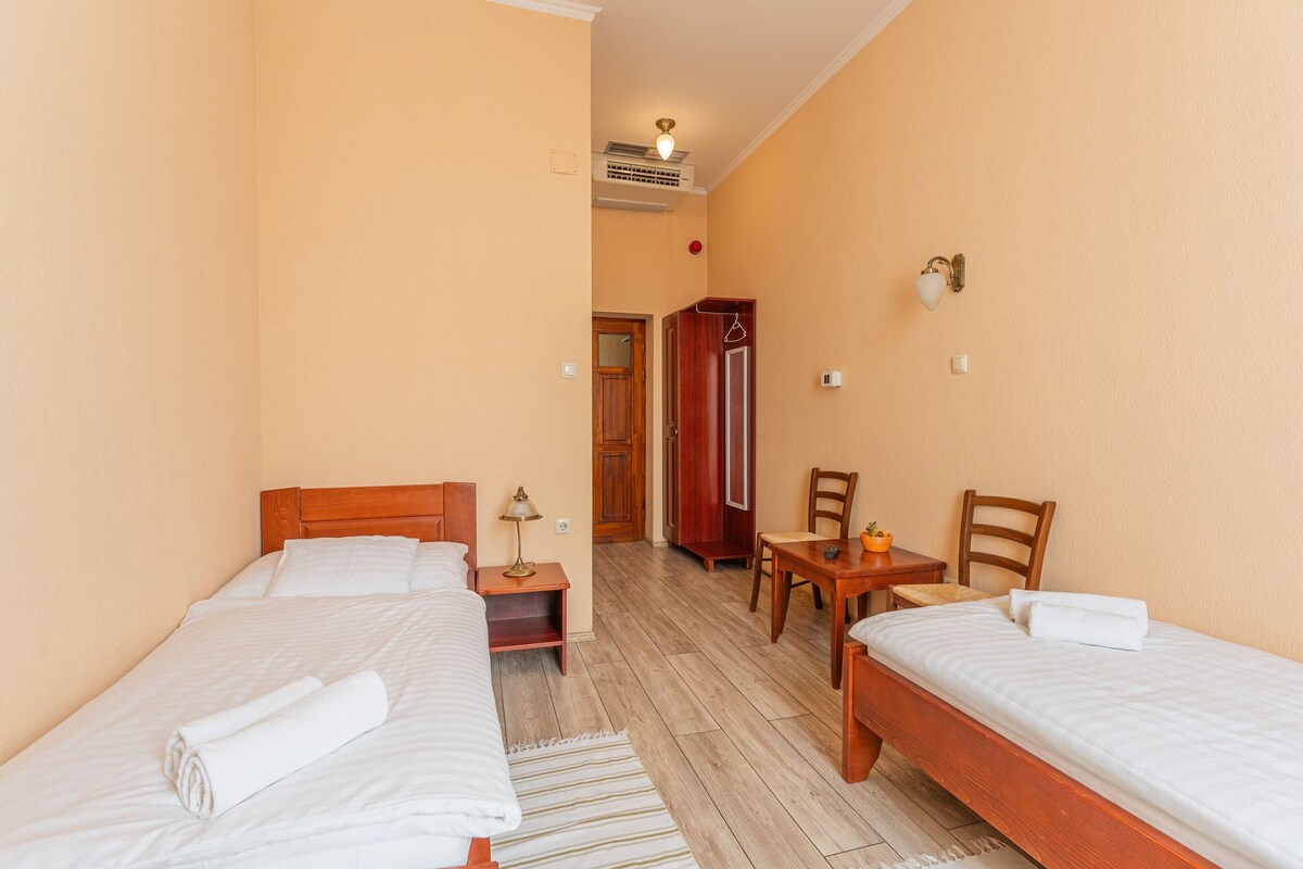 Ein Hotelzimmer mit zwei Einzelbetten, einem Holztisch, einem Stuhl, einem kleinen Tisch und einem Kleiderschrank.