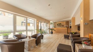A spacious lobby with leather sofas, a reception desk, and large windows. - Oázis Hotel Apartments (Nagykanizsa)