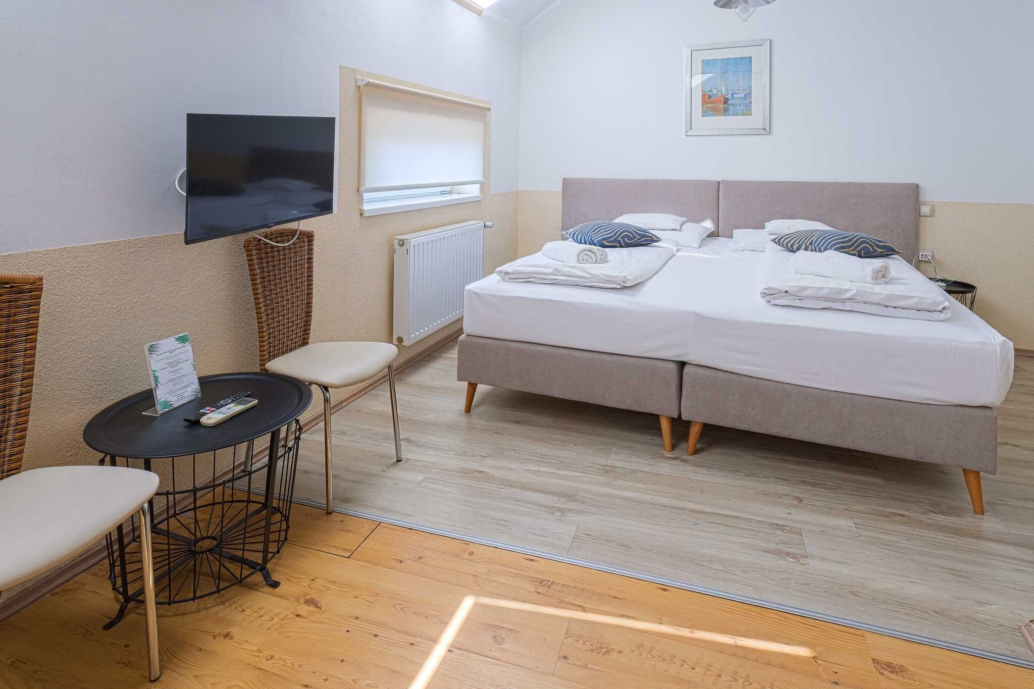Ein Schlafzimmer mit einem Bett, einem an der Wand montierten Fernseher, einem kleinen Tisch mit Stuhl und einem Fenster.