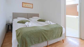 A bed with a green blanket, white pillows, and rolled towels.