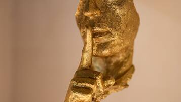Una escultura de figura humana en una pose dinámica, sobre un pedestal rectangular oscuro.
