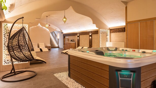 A modern spa room with a hot tub, wooden flooring, and a hanging chair. - Oázis Hotel Apartments (Nagykanizsa)