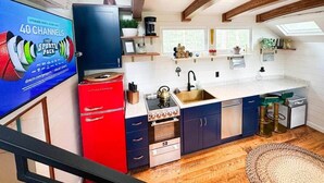 Une cuisine moderne équipée d’une cuisinière à gaz, d’un four et d’un évier. On y trouve un appareil de couleur rouge, un meuble bleu et une fenêtre avec vue.