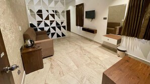 A modern living room with a sofa, a coffee table, a TV mounted on the wall, and a decorative wall panel. - The Lake House (Kodaikanal)