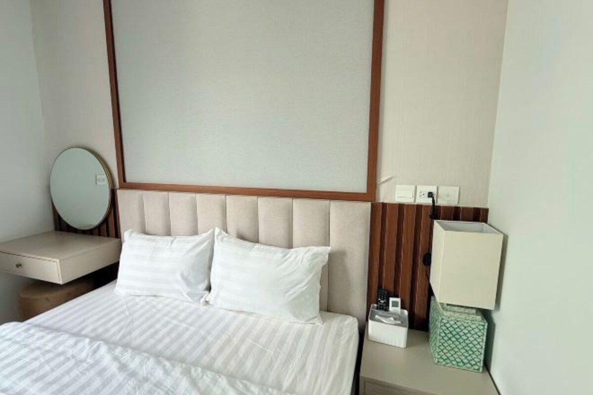 A hotel room with a bed, a bedside table, a lamp, and a mirror.