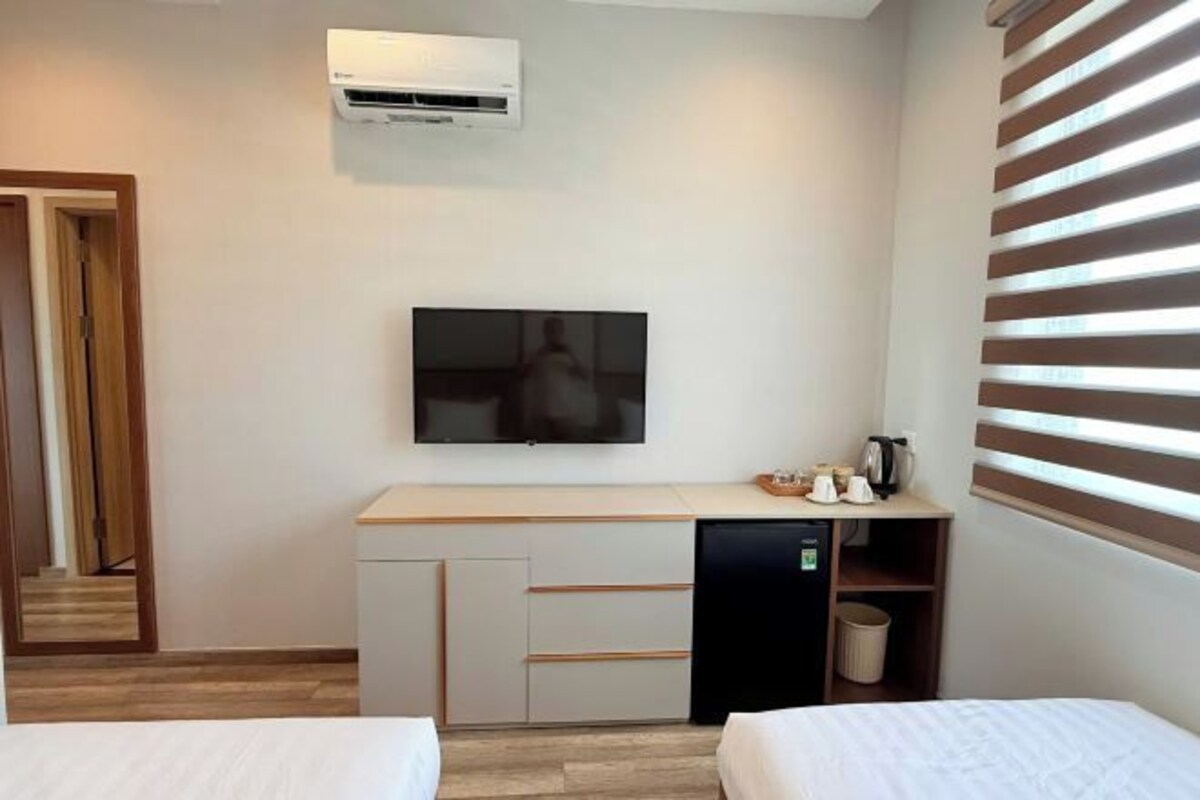 A hotel room with a bed, a desk with a television, an air conditioner, and a window with blinds.