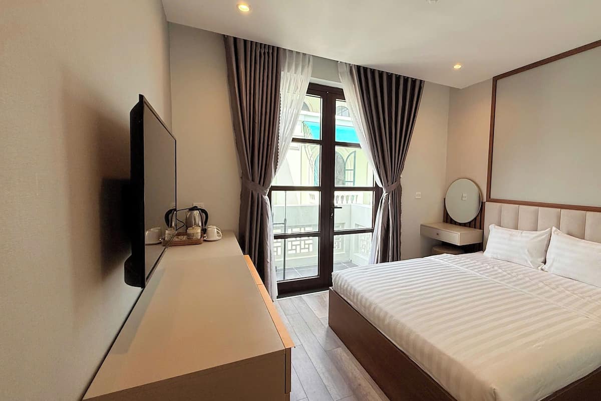 A hotel room with a bed, a bedside table, a TV, a window with curtains, and a view of the outside.