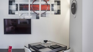 Un espace de repas moderne avec une table dressée pour deux personnes, un téléviseur à écran plat fixé au mur et des œuvres d’art abstraites au-dessus de la table.