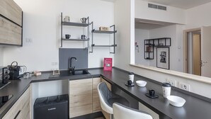 Une cuisine moderne avec un plan de travail noir, un évier encastré et une machine à café. On y trouve deux chaises et une petite poubelle.