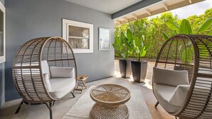 A modern outdoor seating area with wicker chairs and a round table, surrounded by potted plants and a view of lush greenery. - koolkondo 2597 Halalu Guest house (Koloa)