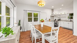 A modern kitchen with white cabinets, a wooden dining table, and a hanging light fixture. - koolkondo 2597 Halalu Guest house (Koloa)
