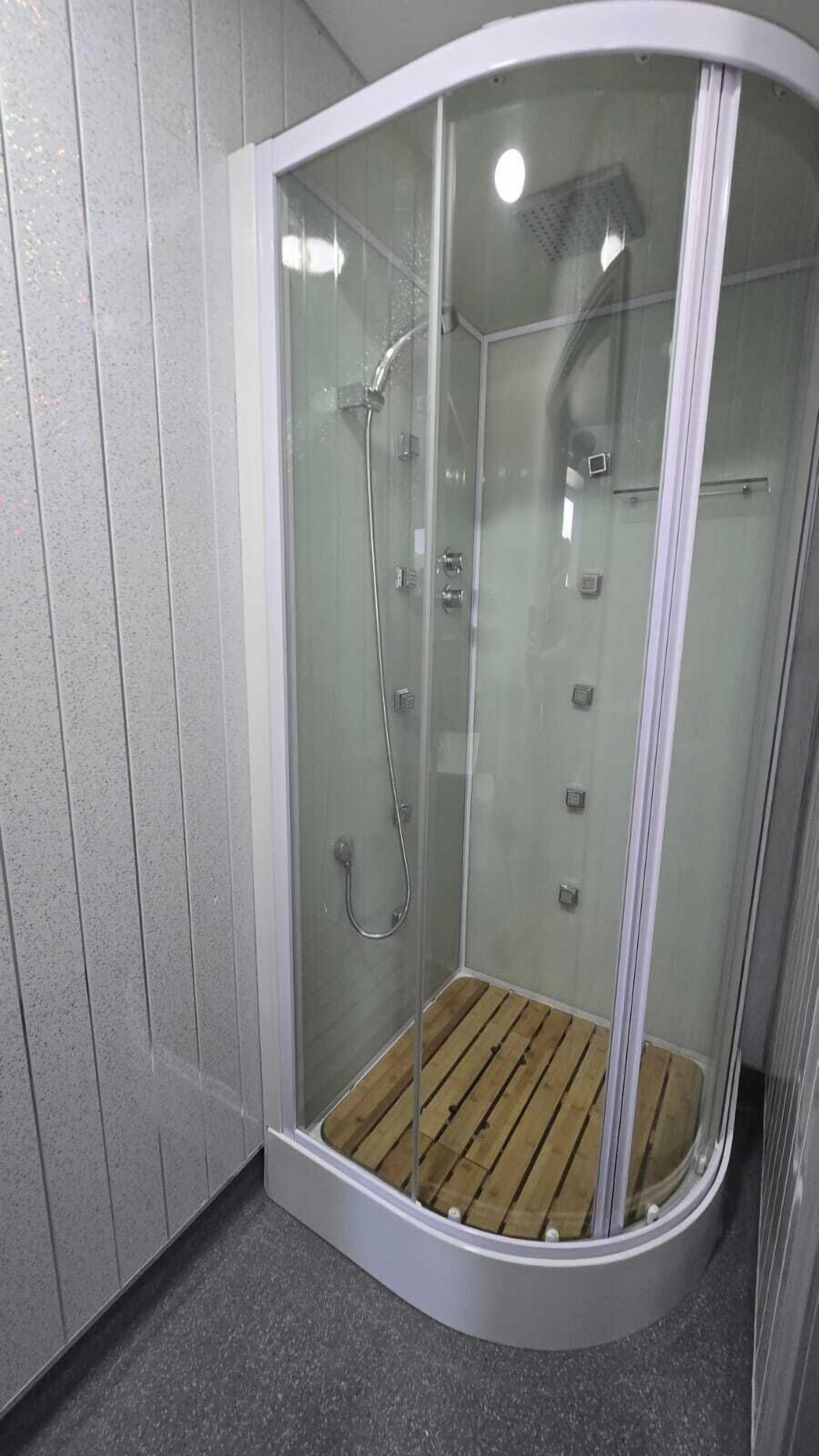 A modern shower enclosure with a glass door, a wooden floor, and a showerhead.