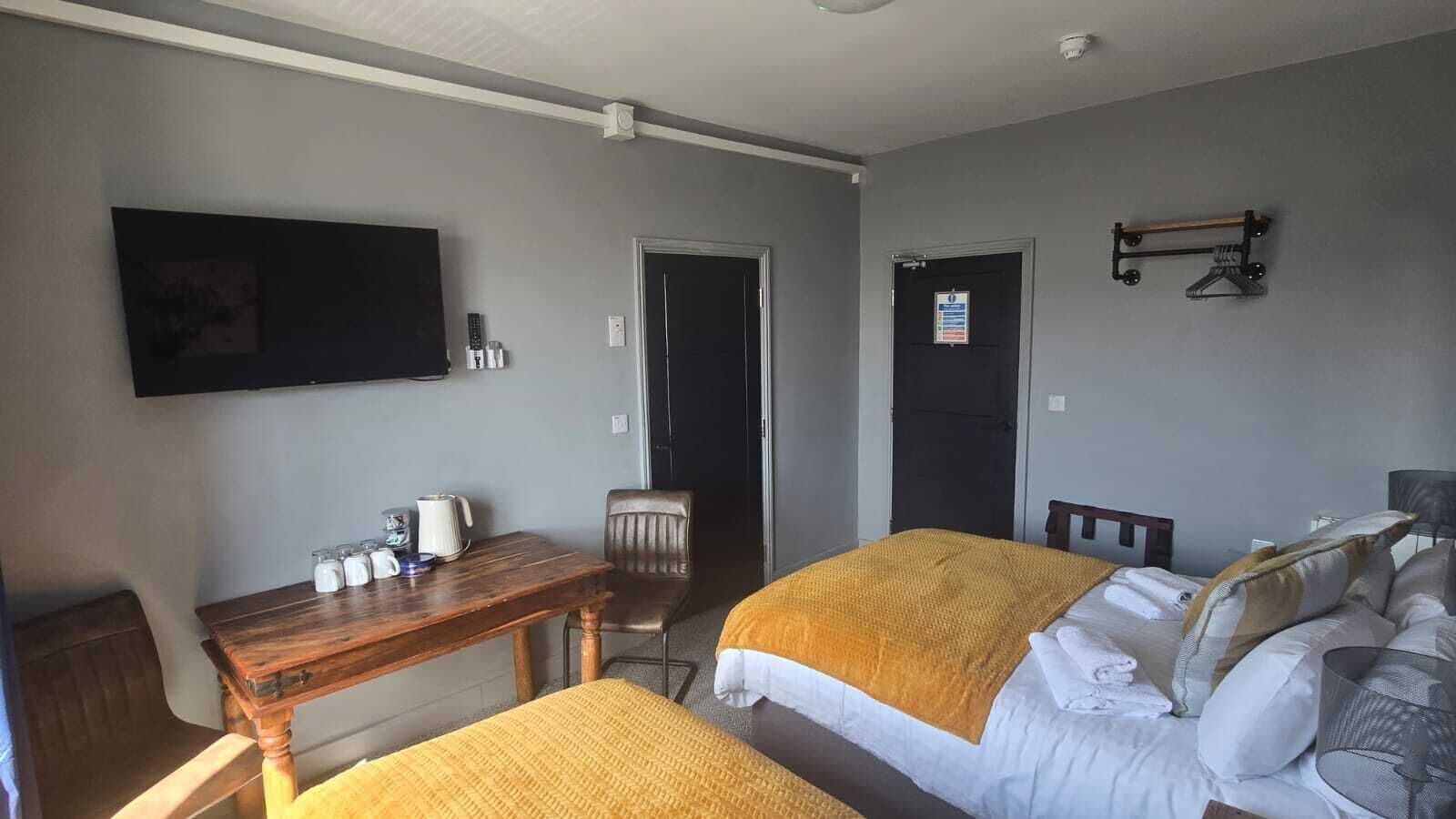 Una habitación de hotel con una cama, una mesa de madera, una silla, un televisor montado en la pared y una puerta con un letrero.