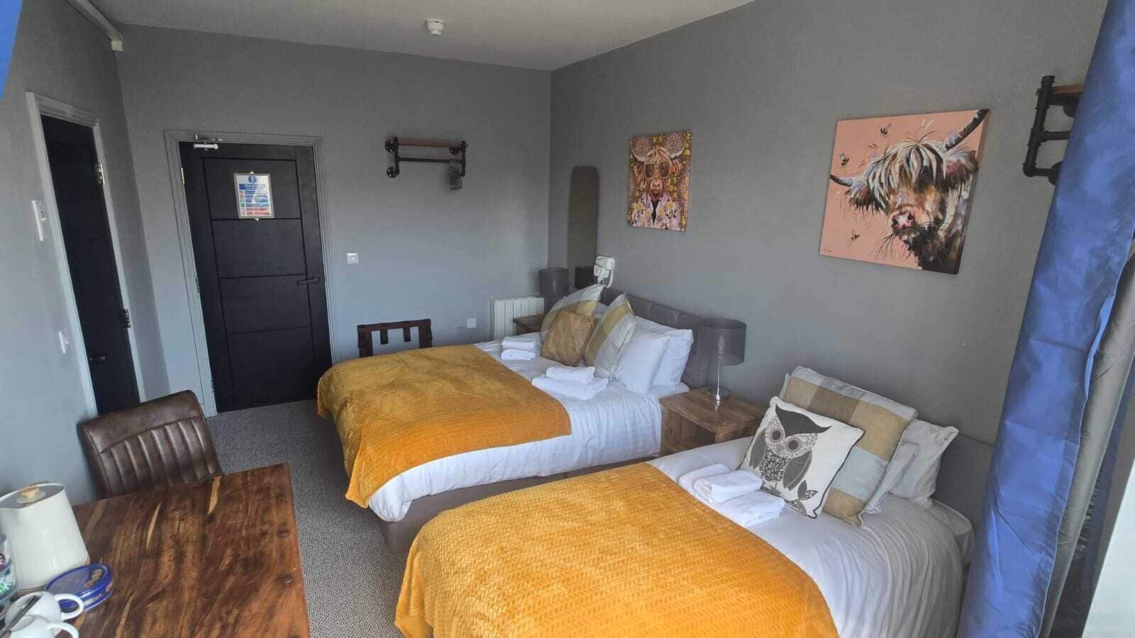 Habitación de hotel con dos camas, un escritorio de madera, una silla y obras de arte en las paredes.