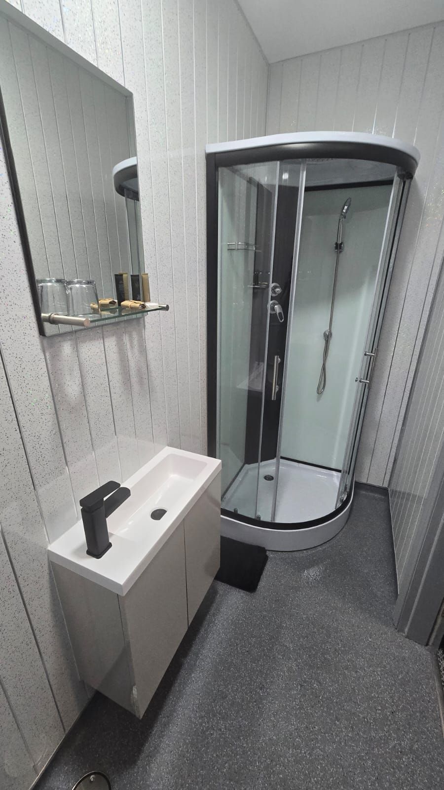 A modern bathroom with a glass-enclosed shower, a white sink with a black faucet, and a mirror above the sink.