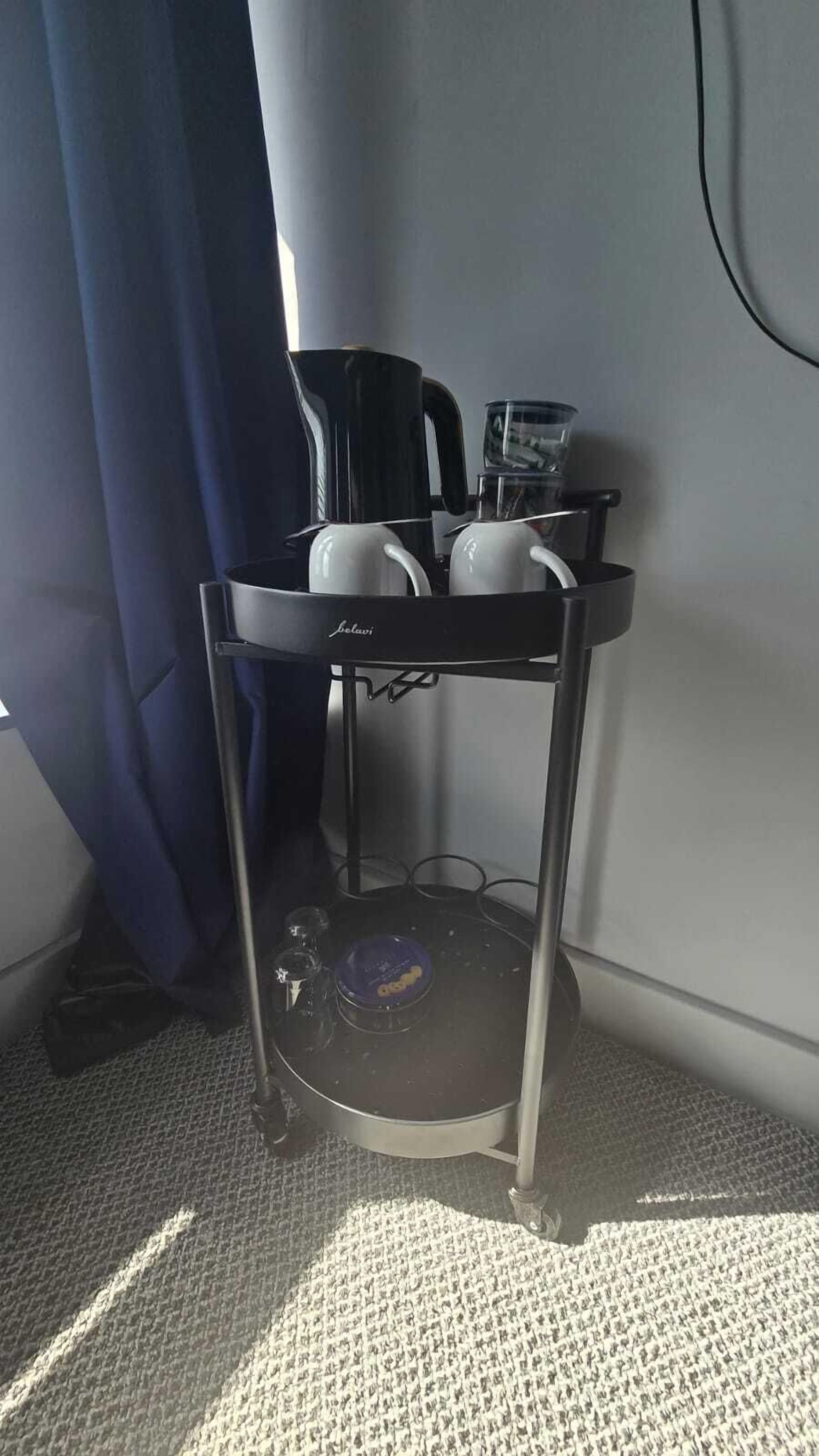 Een kleine kitchenette met een koffiezetapparaat, een waterkoker en een pan op een metalen trolley.