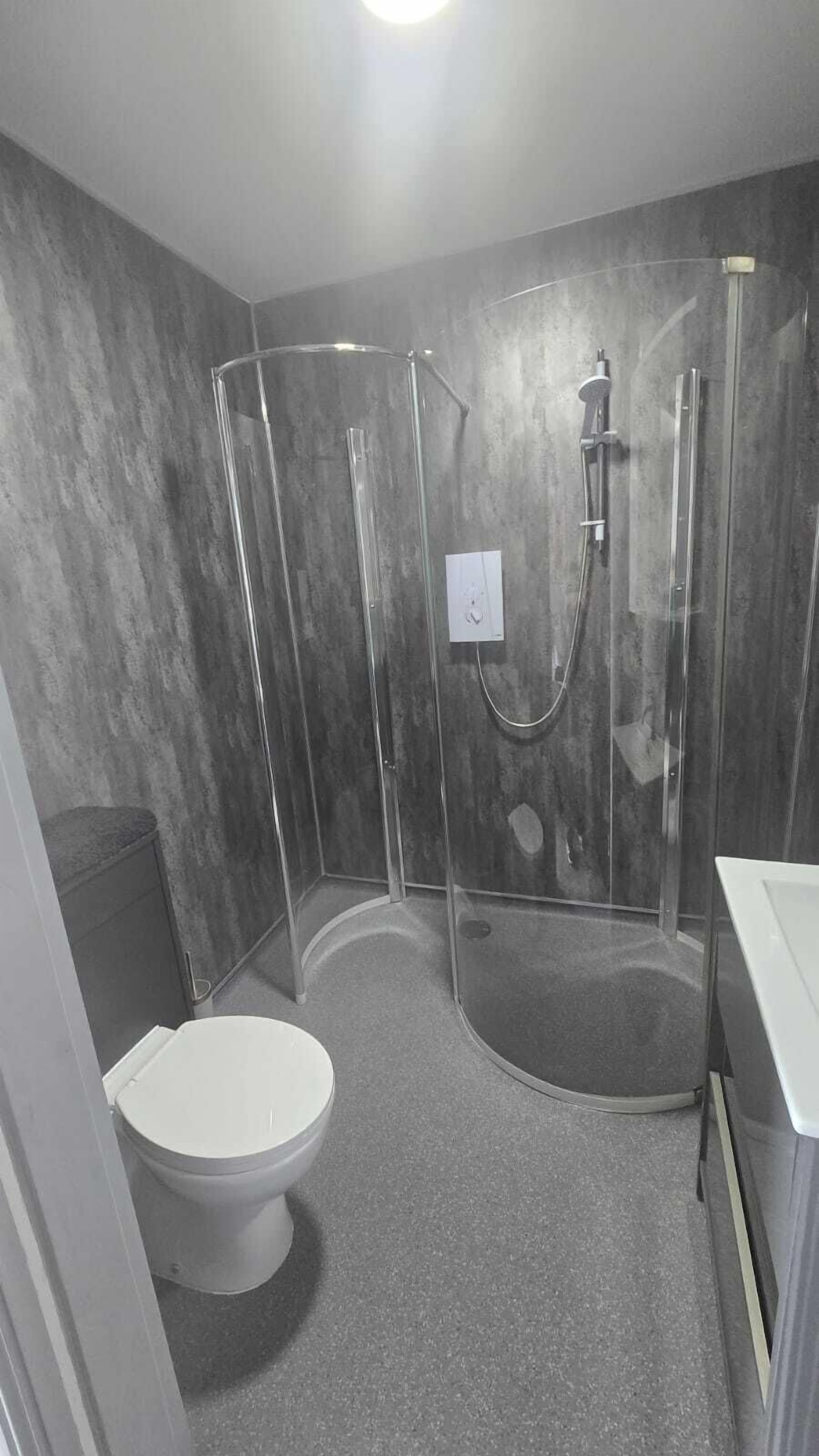 Une salle de bain moderne dotée d’une douche à parois de verre, de toilettes et d’un lavabo.