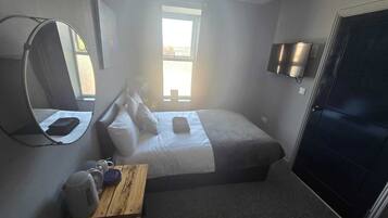 Habitación de hotel pequeña con una cama, una mesita con una taza y un plato, un espejo, un televisor y una puerta.