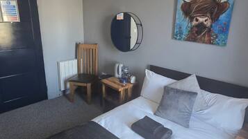 A hotel room with a bed, a chair, a small table with a coffee maker, a round mirror, and a painting on the wall.