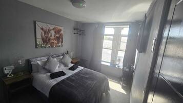 Un dormitorio con cama, mesitas de noche, una lámpara de pared, una ventana con cortinas y una puerta.