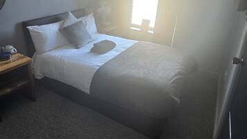 A hotel room with a bed, a nightstand, a painting on the wall, and a window.