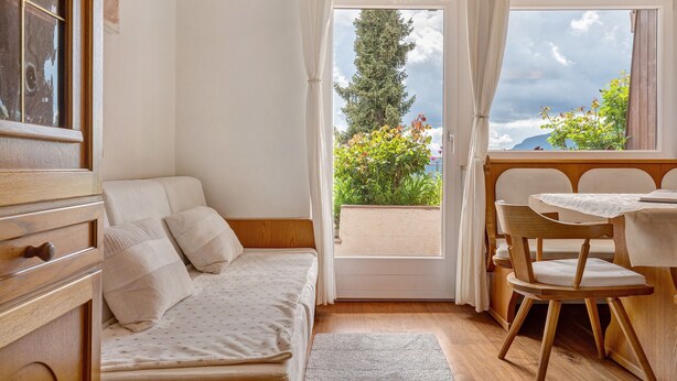 Ein Zimmer mit einem Bett, einem Tisch mit Stühlen, einem Fenster mit Vorhängen und Blick auf Grünflächen und Berge.