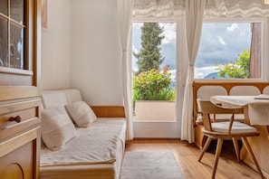 Een kamer met een bed, een tafel met stoelen, een raam met gordijnen en uitzicht op groen en bergen.