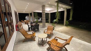 Un espace extérieur aménagé en terrasse, avec des meubles en bois, notamment des chaises et une table, entouré de plantes en pot et équipé d’un extincteur.