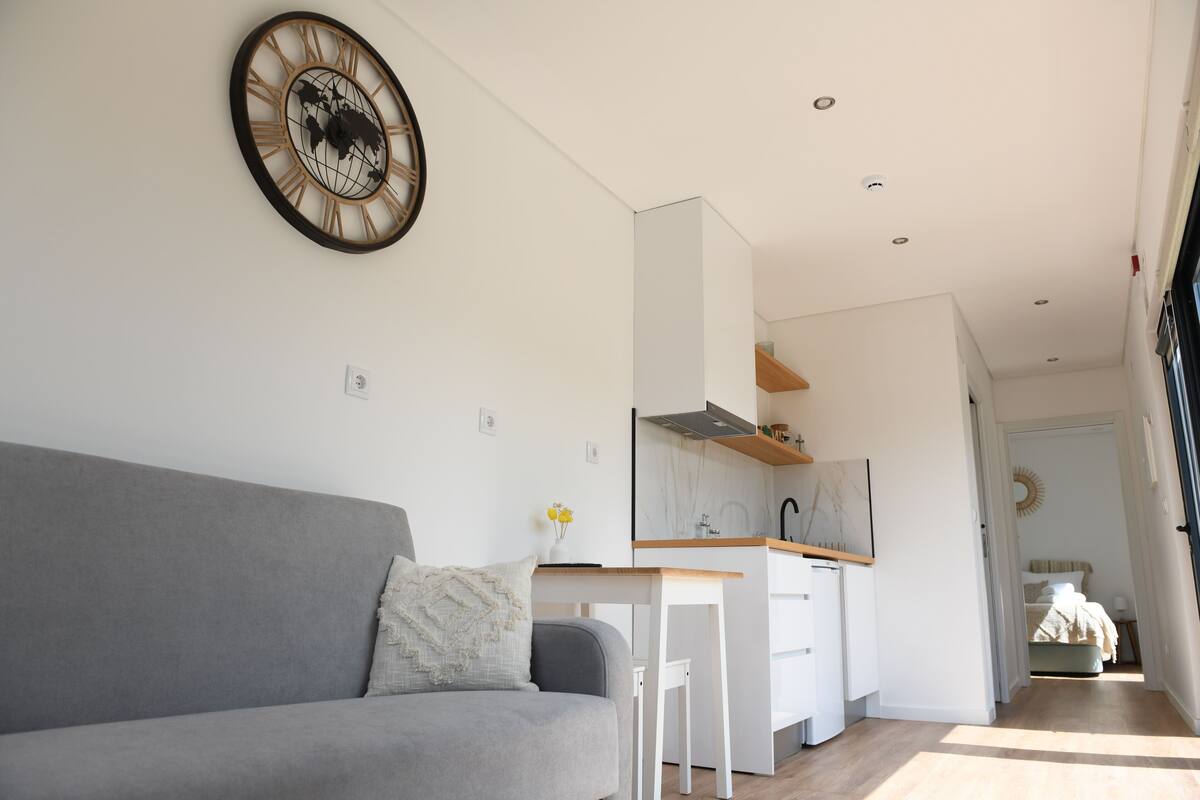 Una sala de estar moderna con un sofá gris, una mesita y una cocina con armarios blancos y una encimera de madera.