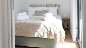 Ein Schlafzimmer mit Bett, Nachttisch, Wandspiegel und Fenster.