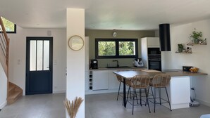 A modern kitchen with a dining area, featuring a large window, a coffee machine, and a built-in oven. - Bright house (Pornic)