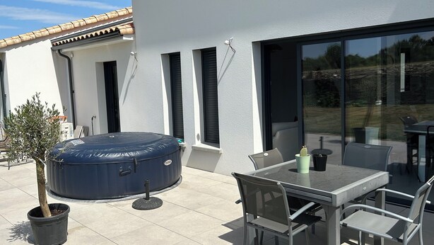 An outdoor patio with a glass table and chairs, a hot tub, and a potted tree. - Bright house (Pornic)