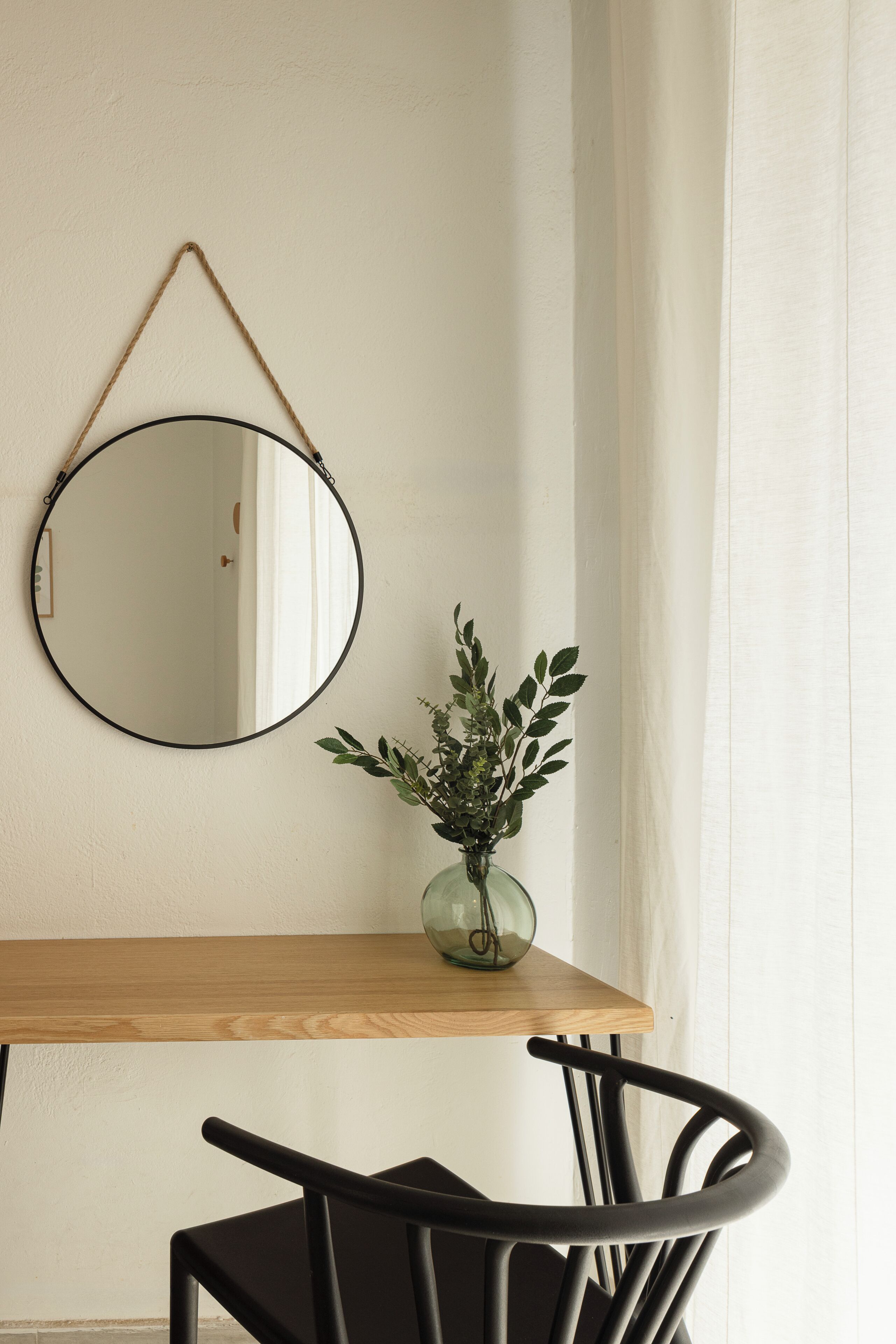 A wooden table with a mirror and a vase with green plants.