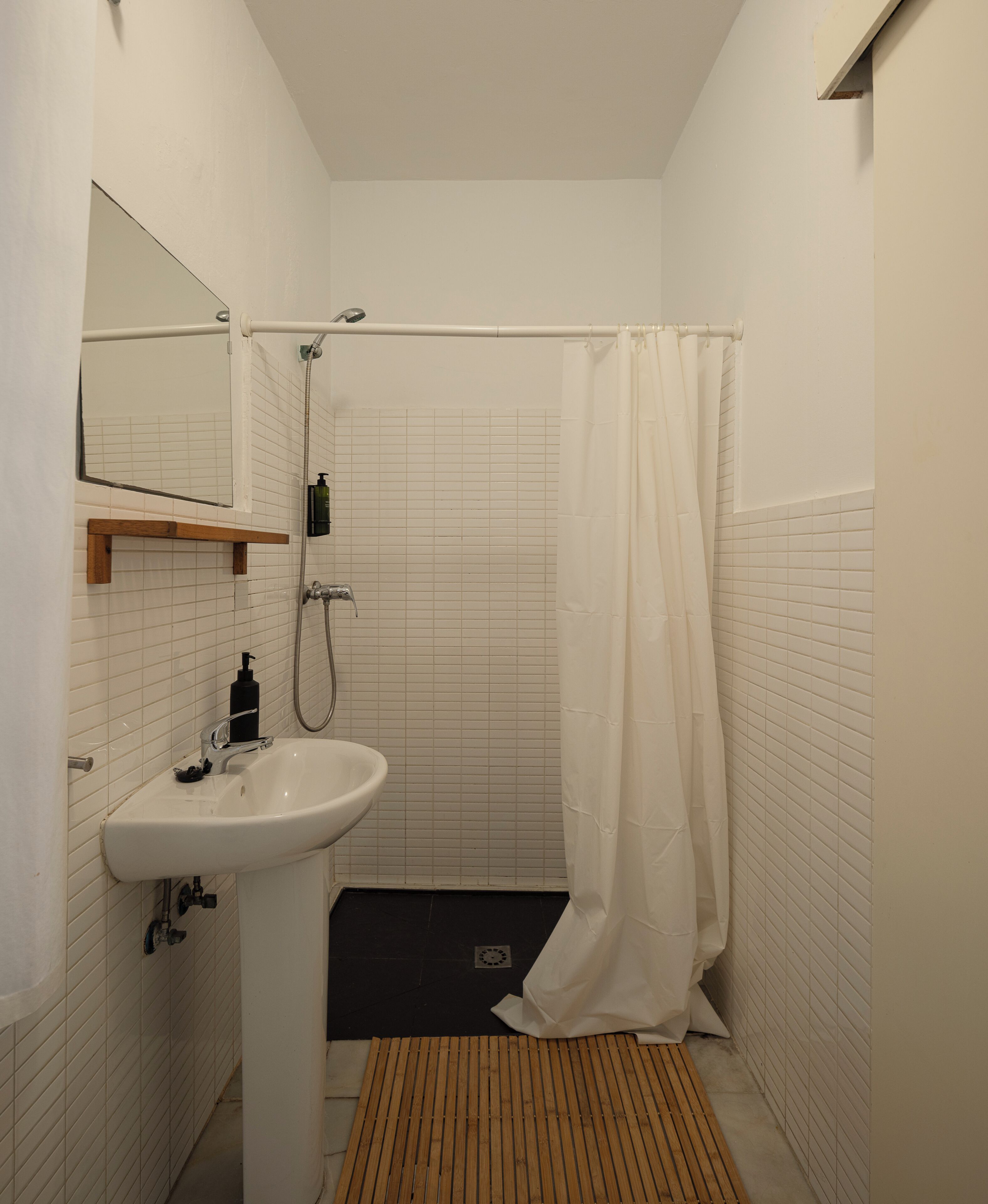 Un baño con lavamanos blanco, espejo y cortina de ducha.