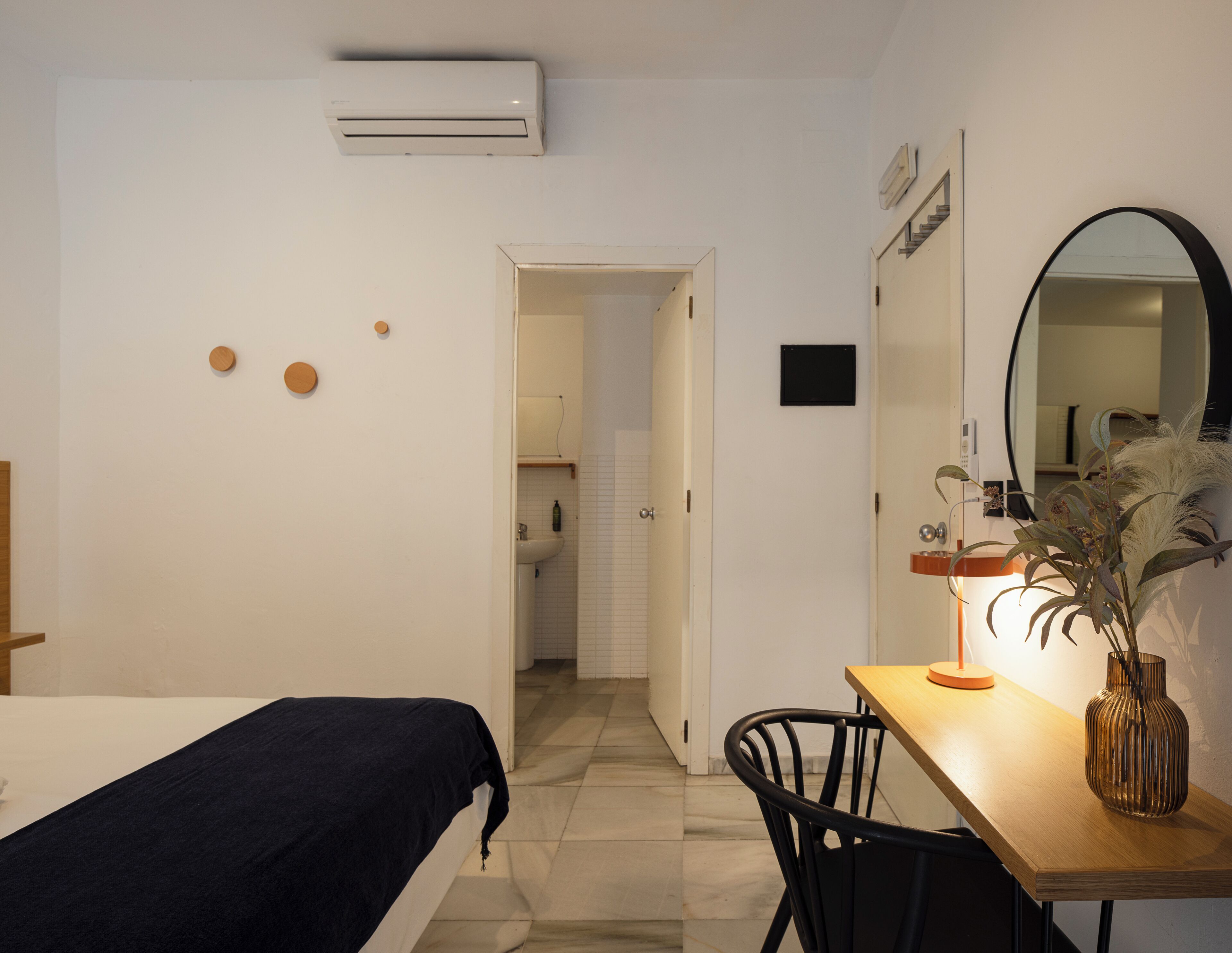 A bedroom with a bed, a desk with a lamp, a mirror, and a potted plant.
