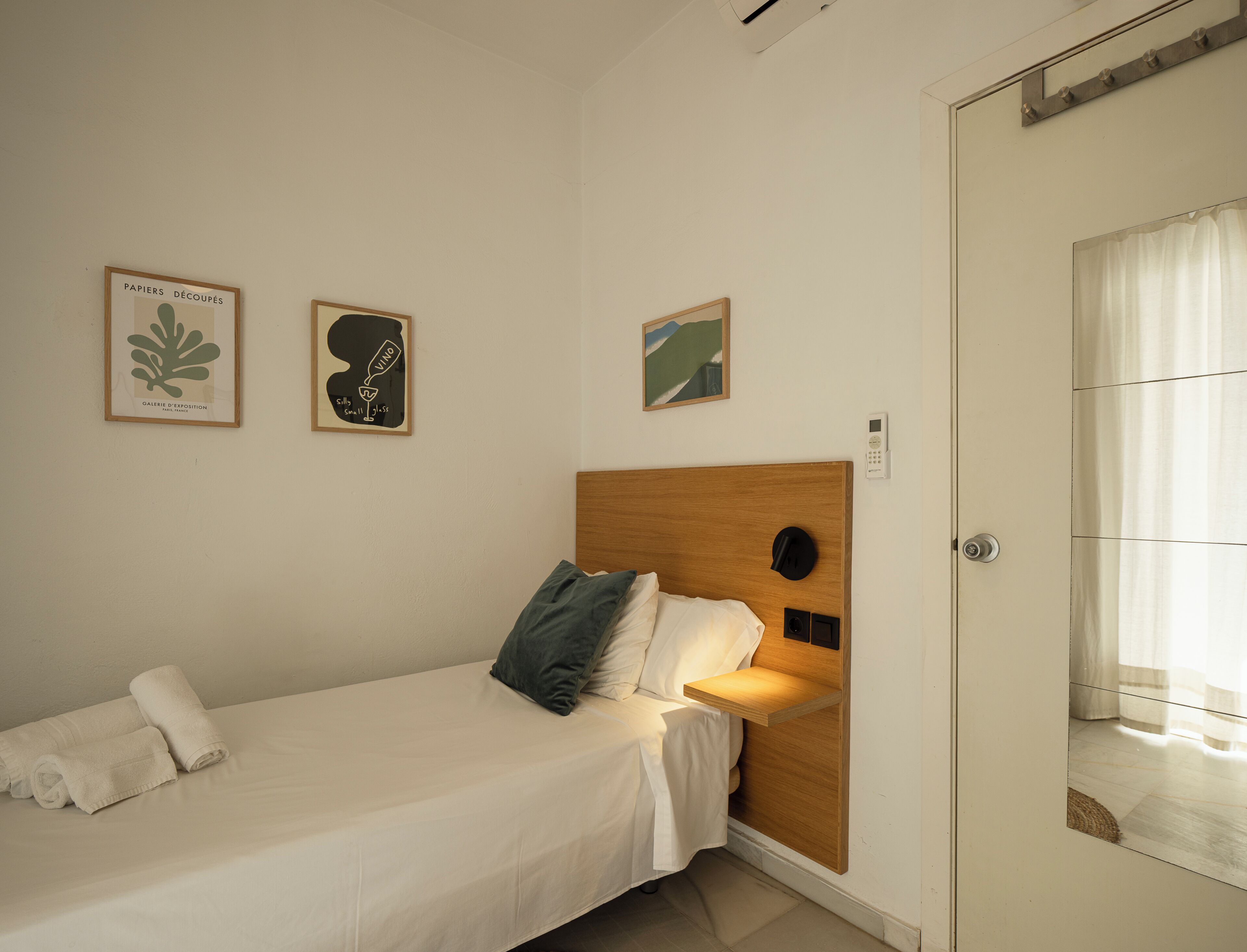 Une chambre à coucher comprenant un lit, une table de chevet, une lampe fixée au mur et une porte dotée d’un miroir.
