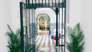 A hallway with a checkered floor leading to a room with a bed and a table. There are two potted plants on either side of the entrance. - La Central Sevilla (Seville)