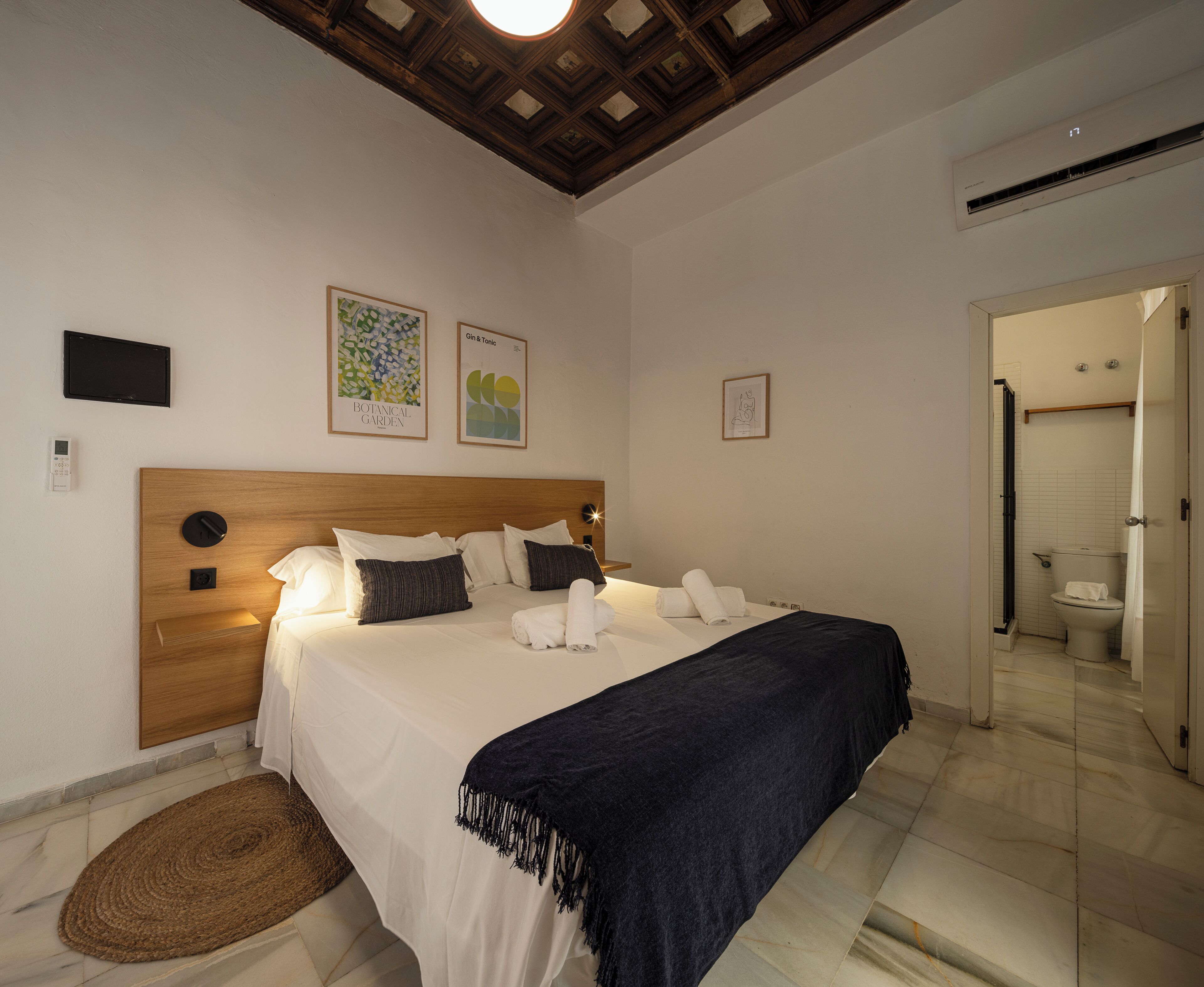 Een hotelkamer met een houten hoofdeinde, een bed met witte lakens, een donkerblauwe plaid, een klein vloerkleed en kunst aan de muren.