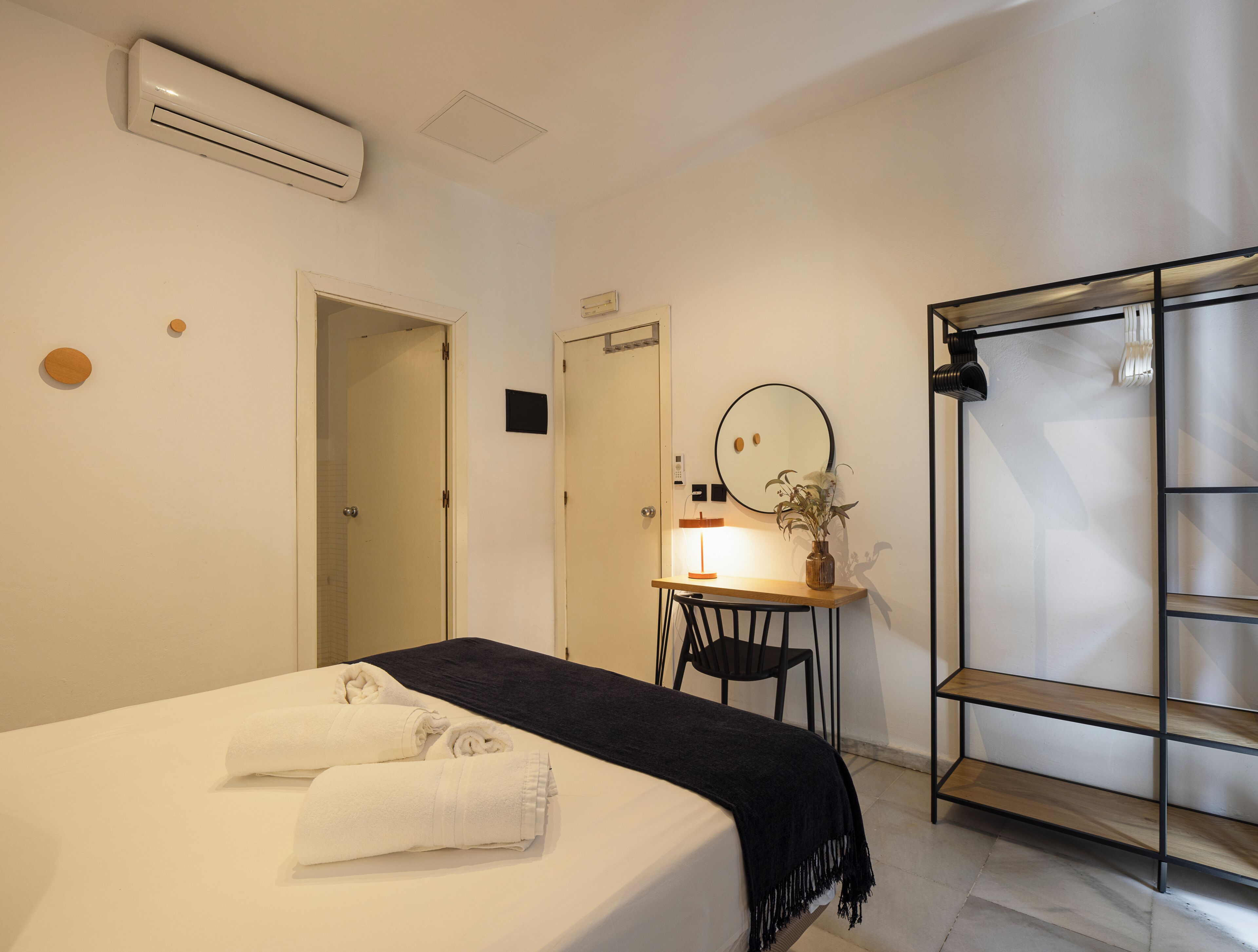 A hotel room with a bed, a desk with a chair, a mirror, and a wardrobe.