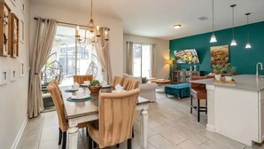 A modern kitchen with a dining area, a teal accent wall, and a hanging light fixture.