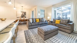 A modern living room with a grey sofa set, a dining area with a white table, and a patterned rug.