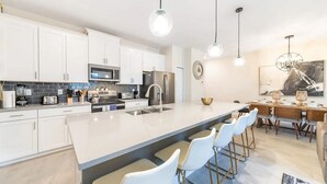 A modern kitchen with white cabinets, stainless steel appliances, and a central island with bar stools.