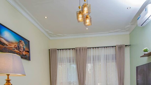 A living room with a sofa set, a smaller sofa, a coffee table, a lamp, a TV, and curtains. - Urban Oasis (Kampala)