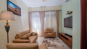 A living room with a sofa, armchair, and a TV on a wooden stand. - Urban Oasis (Kampala)