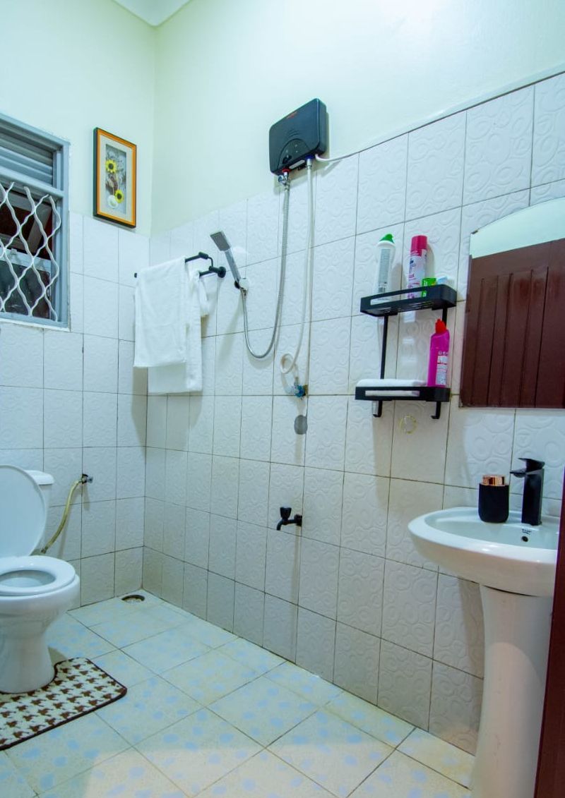 Un baño con inodoro, ducha, lavamanos y una ventana con reja de metal.